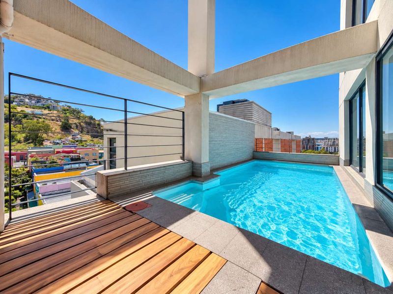 A modern penthouse terrace featuring a private swimming pool, timber decking, and panoramic urban views framed by structural concrete pillars.
