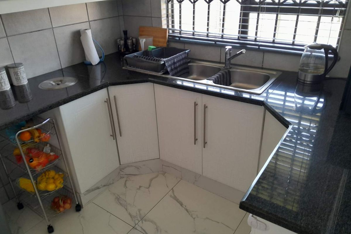 A functional kitchen area featuring dark granite countertops, white cabinetry, a double stainless steel sink, and modern marble-look floor tiles.