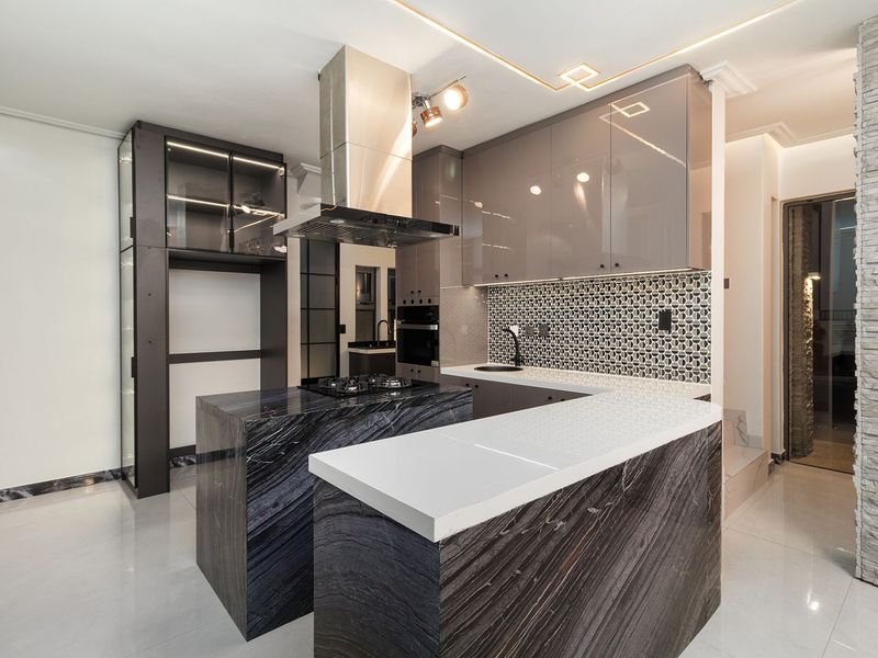 Modern kitchen featuring high-gloss cabinetry, a striking stone island with breakfast bar, integrated appliances, and a decorative mosaic tile backsplash.
