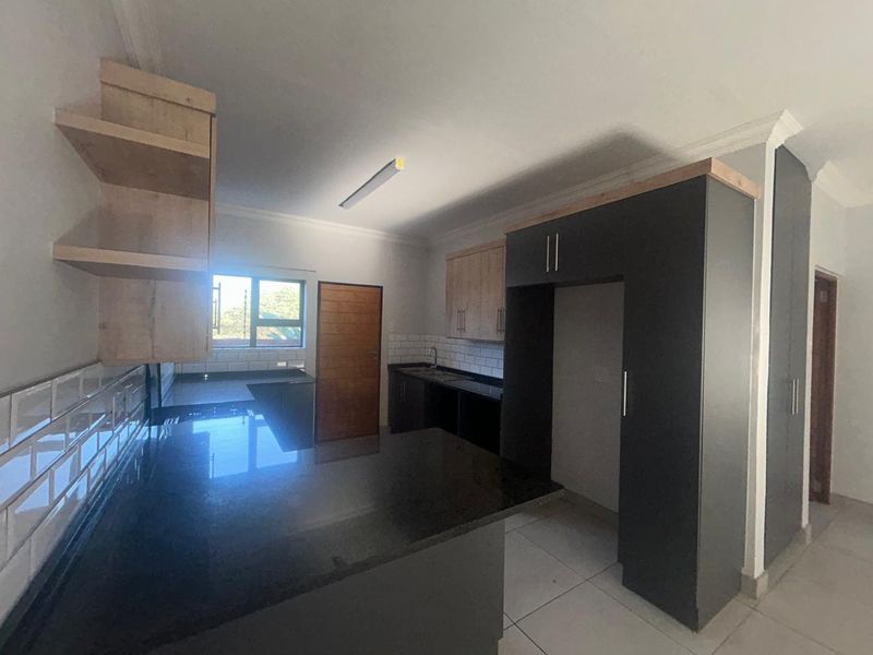 Modern kitchen featuring dark cabinetry, granite countertops, subway tile backsplash, and open shelving, offering a clean and functional workspace.