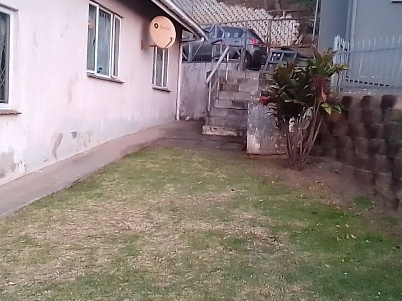 Rear exterior view of the townhouse featuring a small lawn, concrete pathway, retaining wall, and external staircase leading to the upper level.