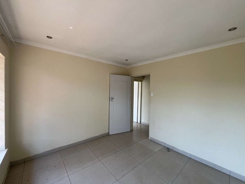 An empty bedroom featuring neutral tiled flooring, recessed downlights, and coved ceilings, providing a blank canvas for personalization.