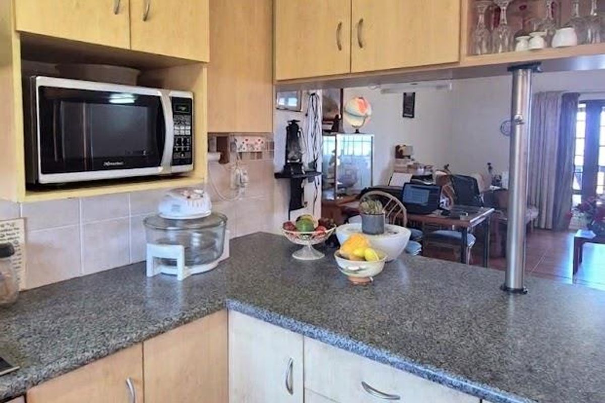 A functional kitchen featuring light wood cabinetry, granite countertops, and a breakfast bar overlooking the living area, with tiled flooring throughout.