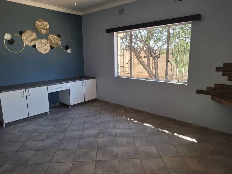 A functional office space featuring built-in cabinetry, tiled flooring, and large windows with security bars, offering a clean and versatile workspace.