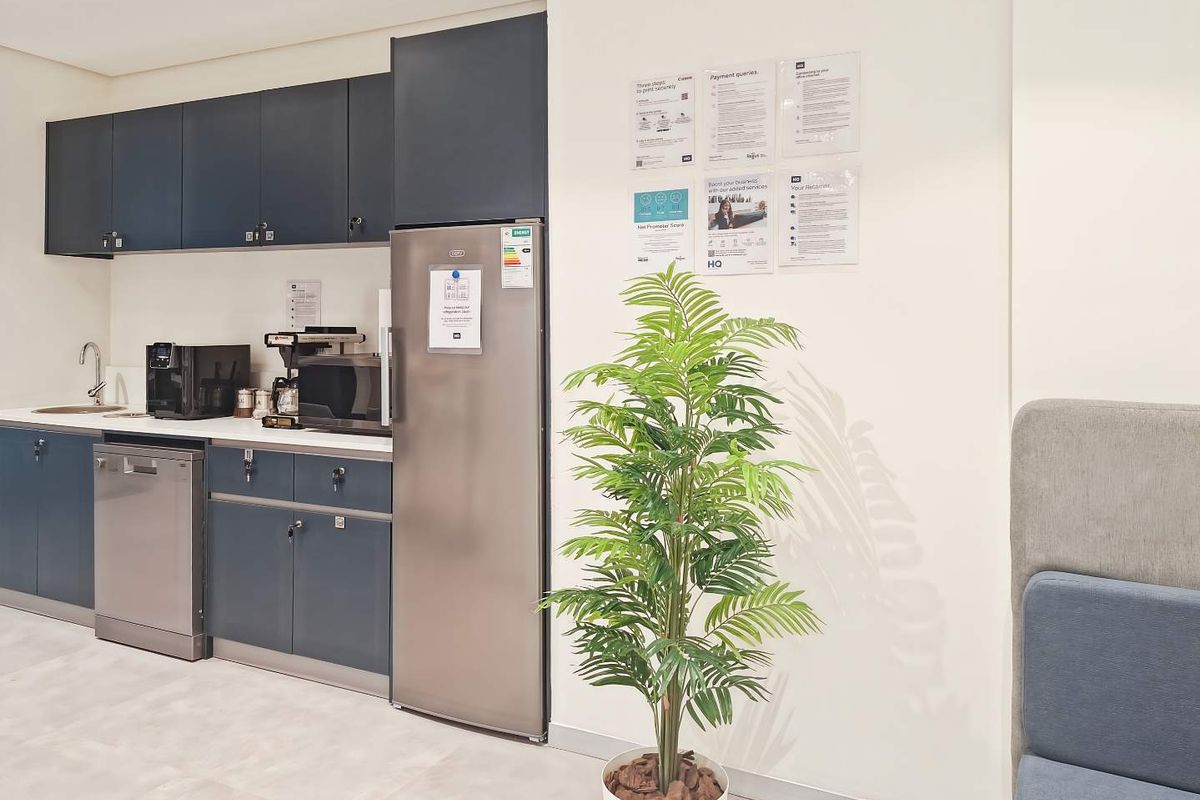 A modern office kitchenette featuring dark blue cabinetry, stainless steel appliances, and a sink, providing a functional break area for staff.
