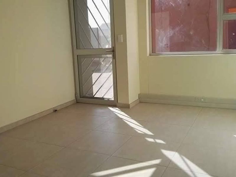 A bright, empty office space featuring tiled flooring, large windows for natural light, and a secure aluminium-framed glass door.