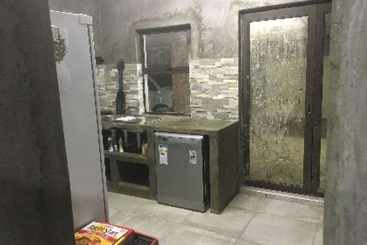 A rustic kitchen area featuring concrete countertops, stone-tiled splashbacks, and a glass door leading to an outdoor space.
