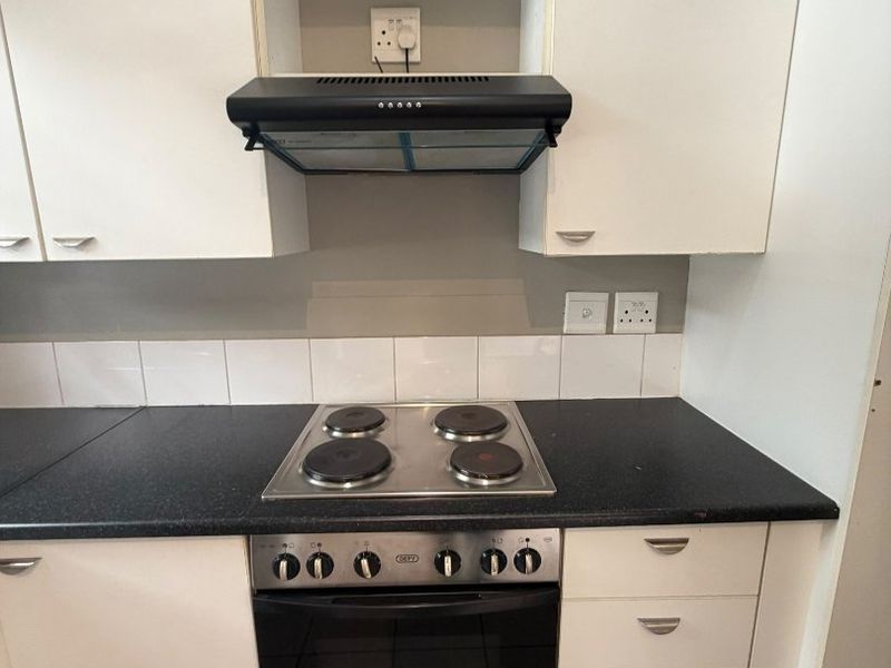 A functional kitchen area featuring built-in cabinetry, a black laminate countertop, an electric hob, an oven, and an extractor fan with tiled backsplash.
