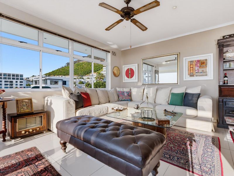 A bright and spacious living room featuring large windows with scenic views, tiled flooring, and a ceiling fan.