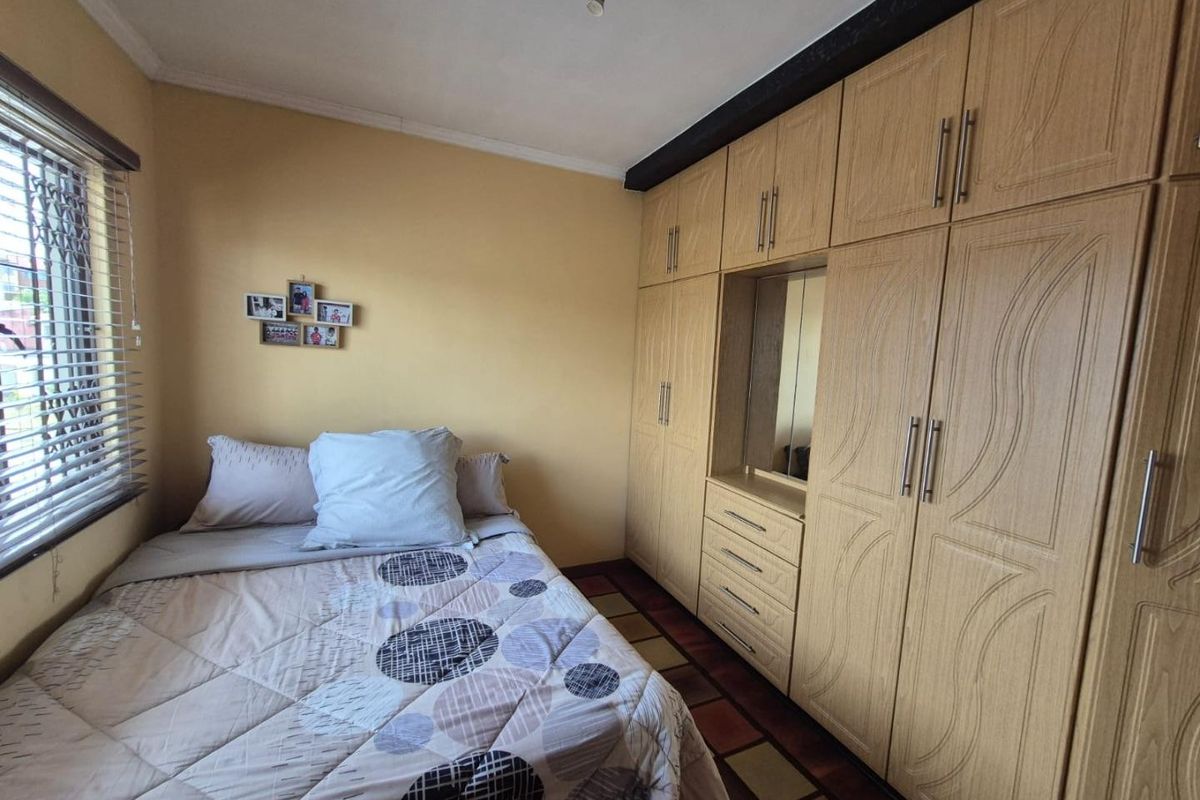 A functional bedroom featuring extensive built-in wooden cabinetry with integrated vanity mirror and venetian blinds for light control.