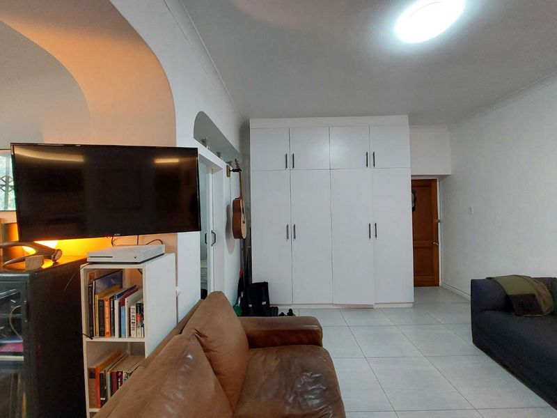 A living room featuring white built-in cupboards, tiled flooring, and a distinctive architectural archway, providing a functional and neutral living space.