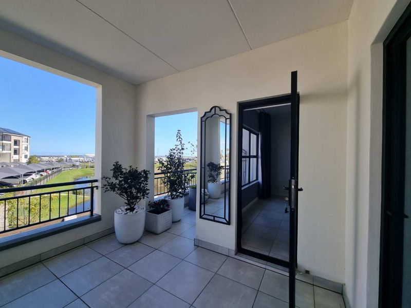 A spacious covered balcony featuring tiled flooring, a metal balustrade, and views over the surrounding estate.