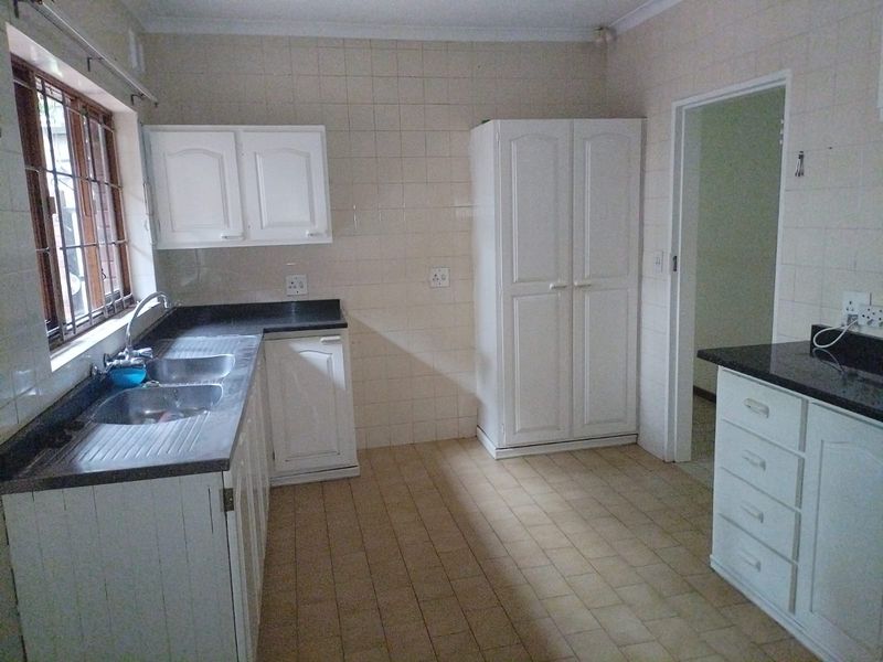 A functional kitchen featuring white built-in cabinetry, granite countertops, a double basin sink, and tiled splashbacks with neutral floor tiles.
