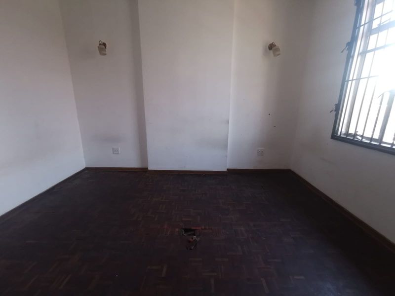 An empty bedroom featuring dark parquet flooring with visible damage and wall-mounted lighting, ready for renovation or staging.