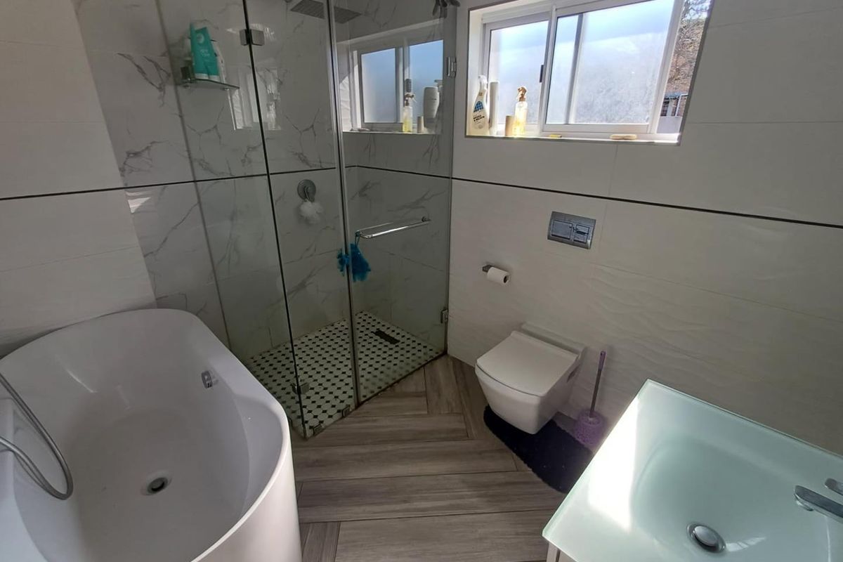 Modern bathroom featuring a glass-enclosed shower, freestanding bathtub, wall-mounted toilet, and a contemporary vanity sink with marble-look wall tiles.