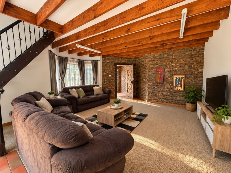 Spacious living room featuring exposed timber ceiling beams, a rustic brick feature wall, and a staircase with wrought iron detailing.