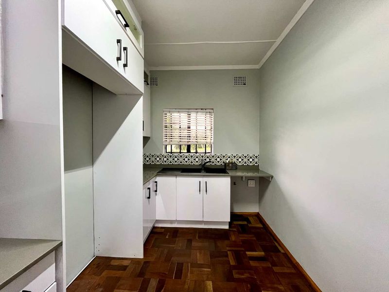 A clean, functional kitchen featuring white built-in cabinetry, a patterned tile backsplash, double sink, and classic parquet flooring.
