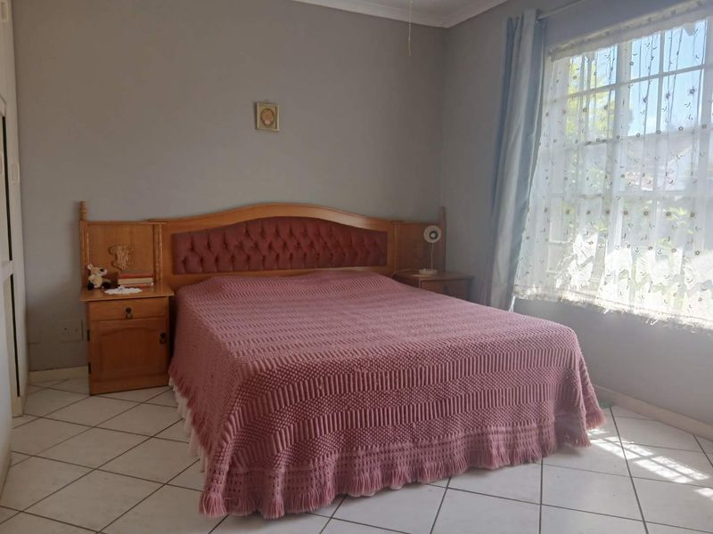 A bedroom featuring tiled flooring and a window with security bars, providing a functional space with neutral wall tones.