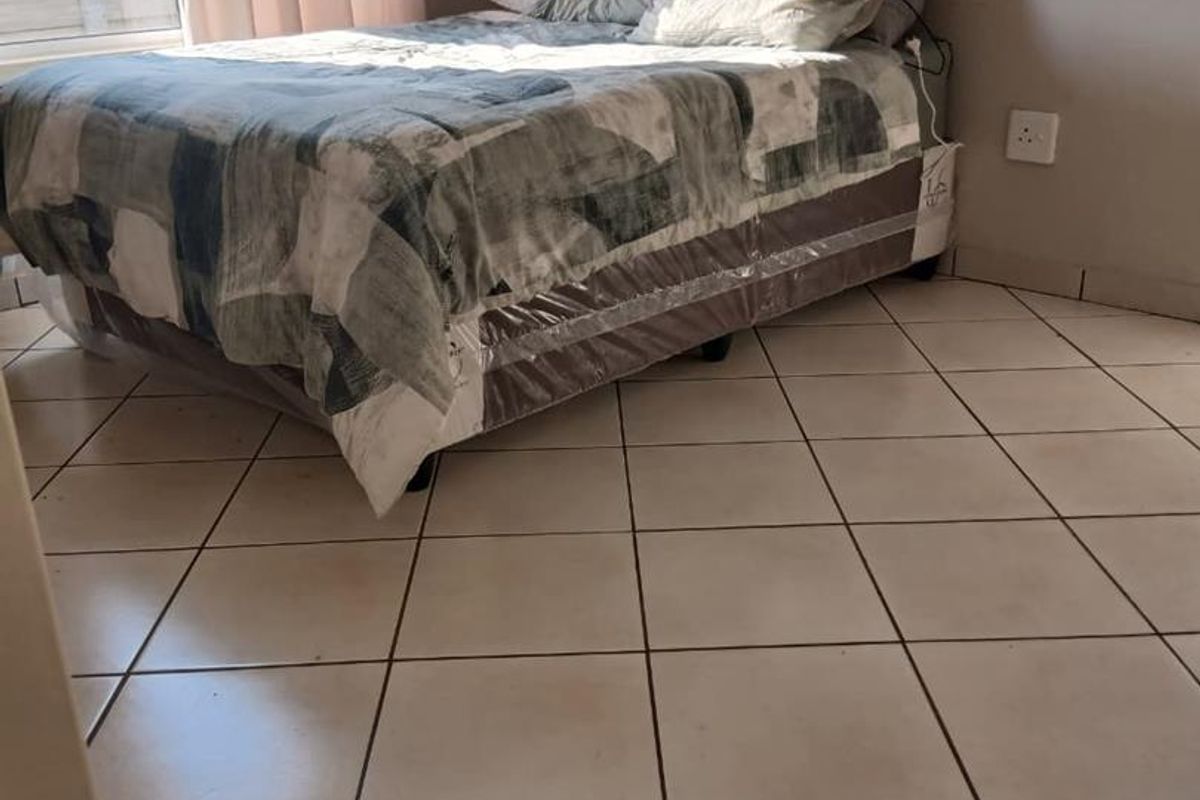 A bedroom featuring tiled flooring and a large window, providing natural light. The space is functional with standard finishes.