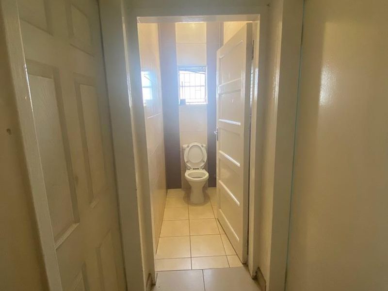 A narrow hallway leading to a small restroom featuring tiled flooring, internal doors, and transom windows above the door frames.