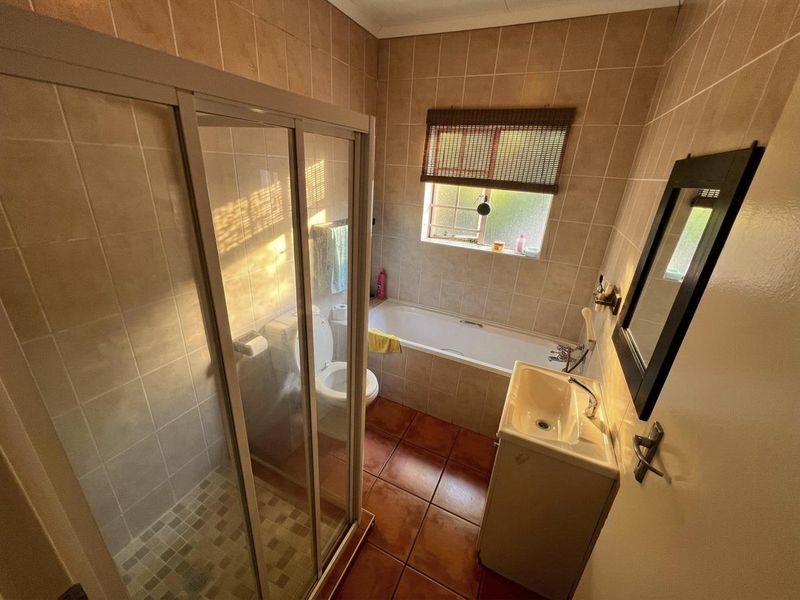 A functional bathroom featuring a shower enclosure, bathtub, and pedestal basin with neutral wall and floor tiling.