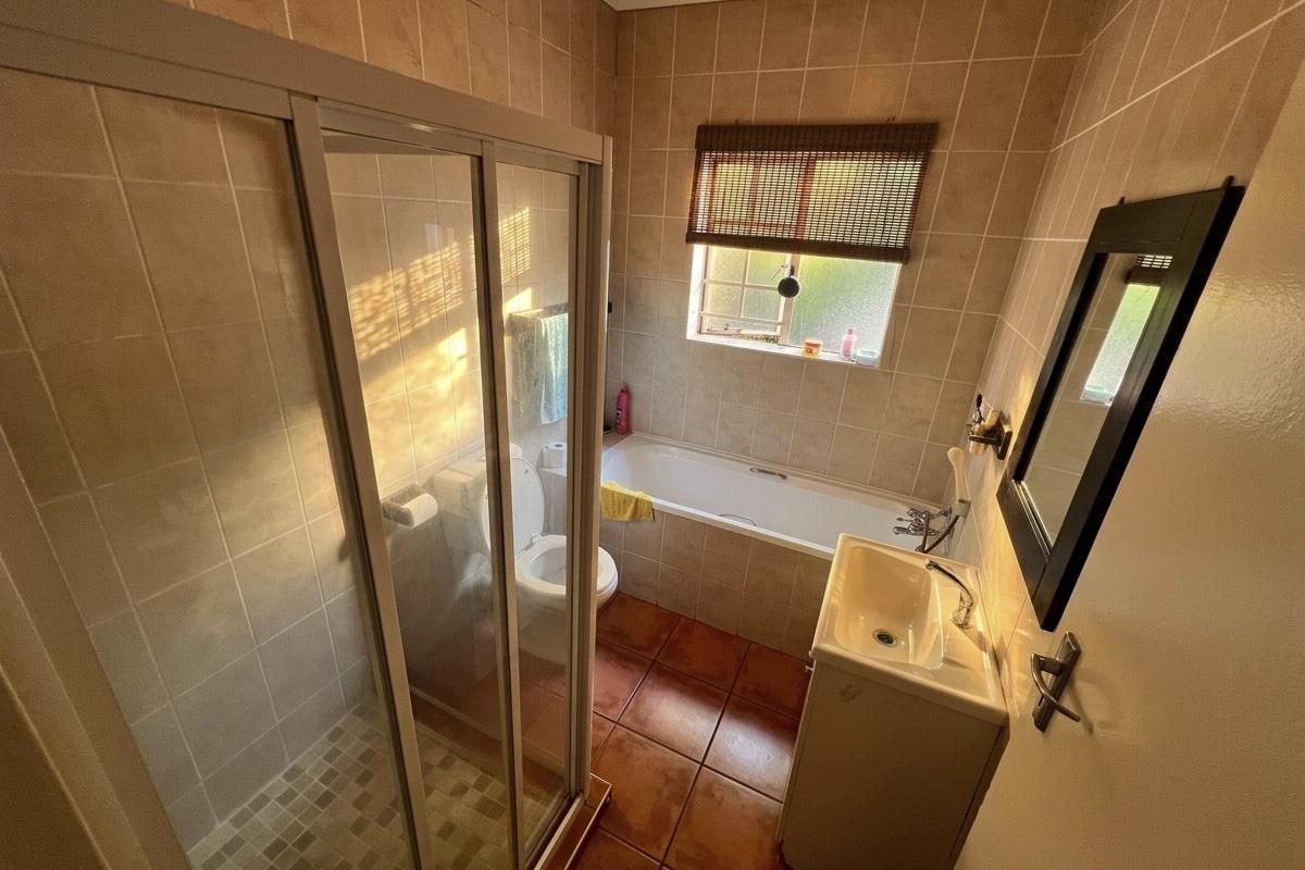 A functional bathroom featuring a shower enclosure, bathtub, and pedestal basin with neutral wall and floor tiling.