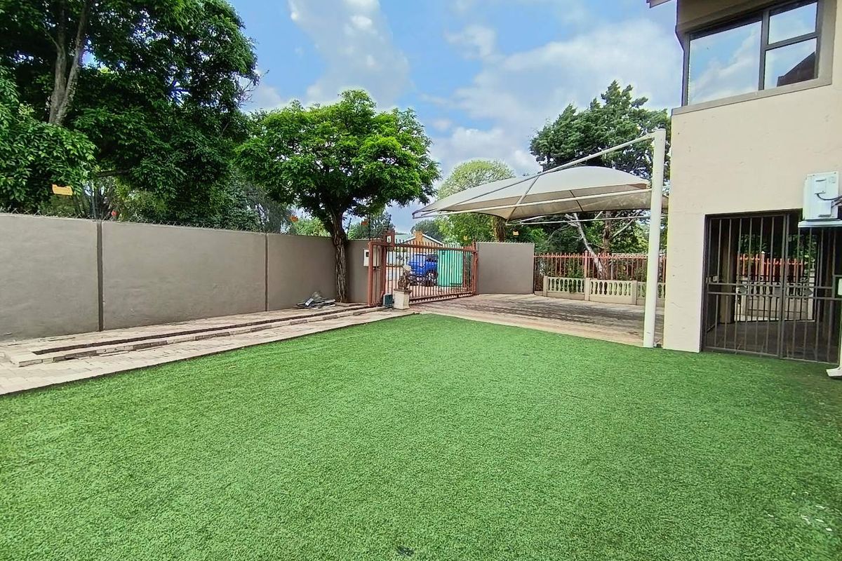 A well-maintained rear garden area featuring artificial turf, a paved driveway section with a shade sail, and secure perimeter walling.