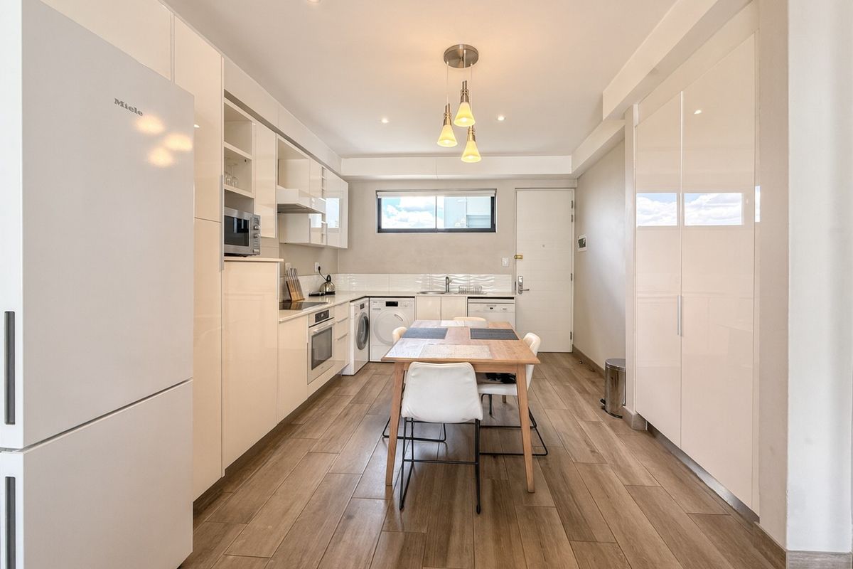 Modern kitchen featuring high-gloss cabinetry, integrated appliances, wood-look tiled flooring, and recessed lighting in a clean, contemporary open-plan layout.