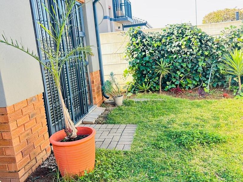A view of the rear exterior featuring a brick and plaster facade, security gate, paved path, and a small private garden area.