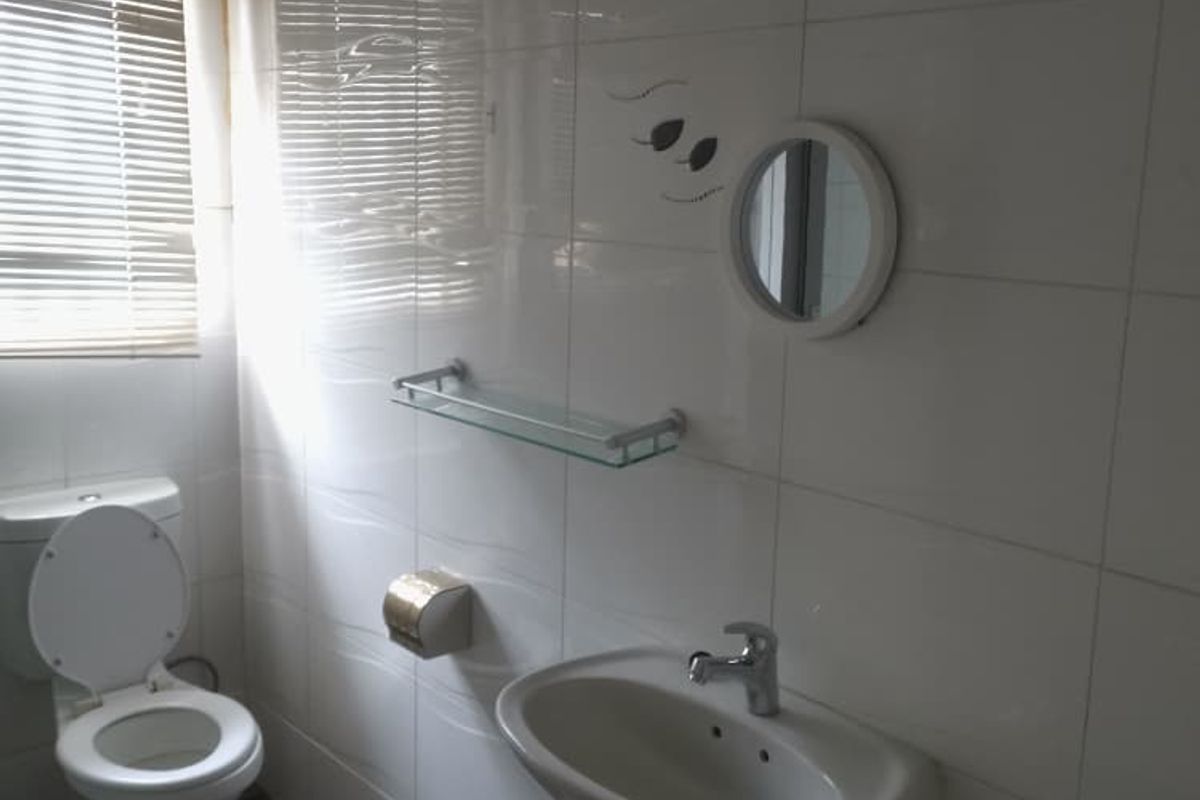 A functional bathroom featuring white wall tiles, a wall-mounted basin, a toilet, and a window with fitted blinds.