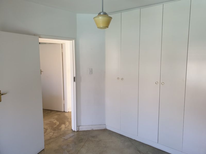A vacant bedroom featuring built-in white cupboards, a pendant light fixture, and exposed concrete flooring, offering a blank canvas for interior design.