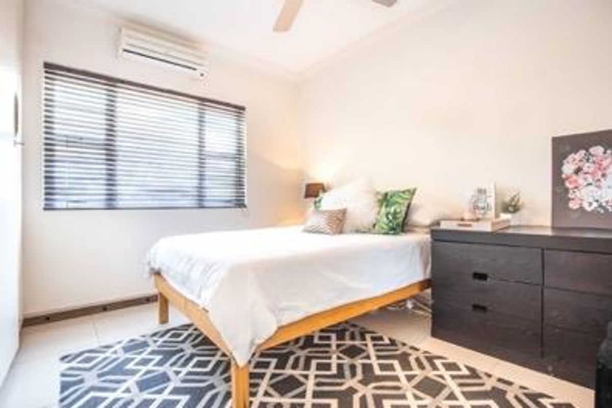 A bright bedroom featuring tiled flooring, a wall-mounted air conditioning unit, and venetian blinds.