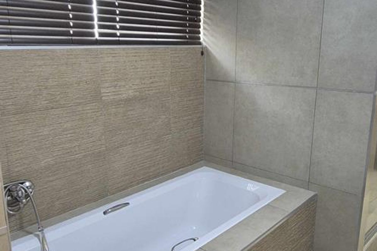 Modern bathroom featuring a built-in bathtub with textured wall tiling, large format floor tiles, and a fitted window blind.