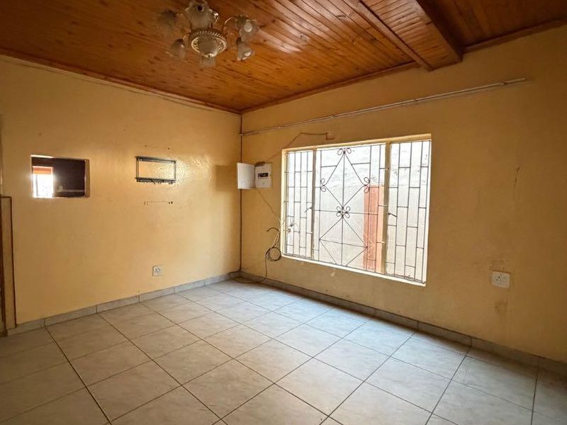 An empty living room featuring a timber-clad ceiling, ceramic tiled flooring, and a window fitted with security bars.