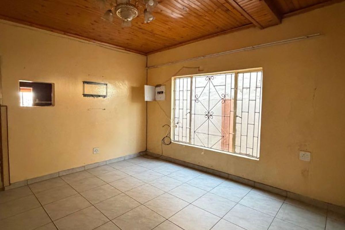 An empty living room featuring a timber-clad ceiling, ceramic tiled flooring, and a window fitted with security bars.