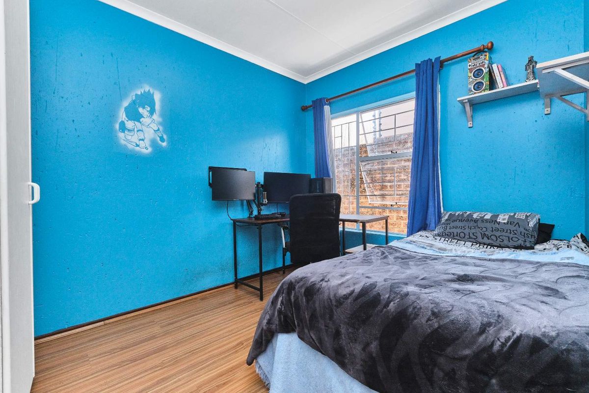 A bedroom featuring laminate flooring and a window with security bars. The room requires cosmetic updates to the wall finishes.