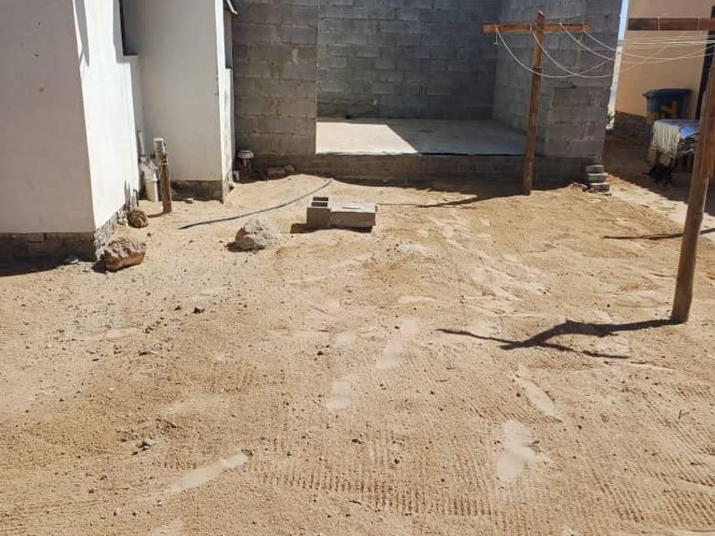 Rear exterior view showing an unfinished concrete block structure extension and an unlandscaped sandy yard area.