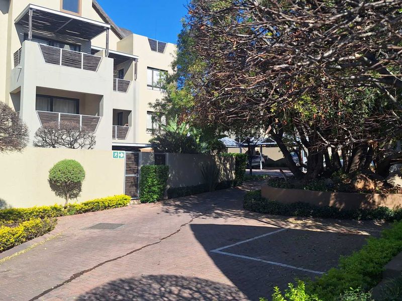 Exterior view of an apartment complex featuring a paved driveway, landscaped garden areas, and multi-level balconies.