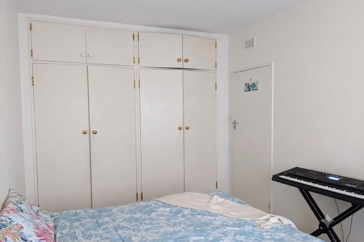 A bedroom featuring floor-to-ceiling built-in cupboards with integrated overhead storage units, providing ample storage space.