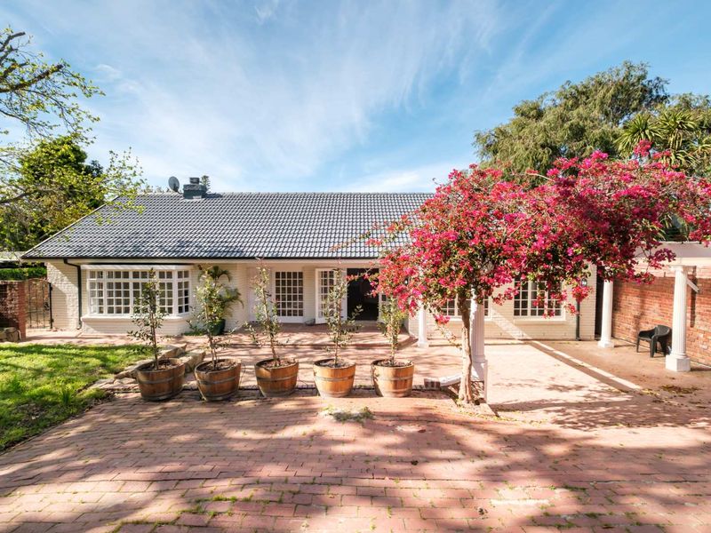 A well-maintained rear exterior view featuring a spacious brick-paved patio, a pergola, and classic french doors leading into the home.