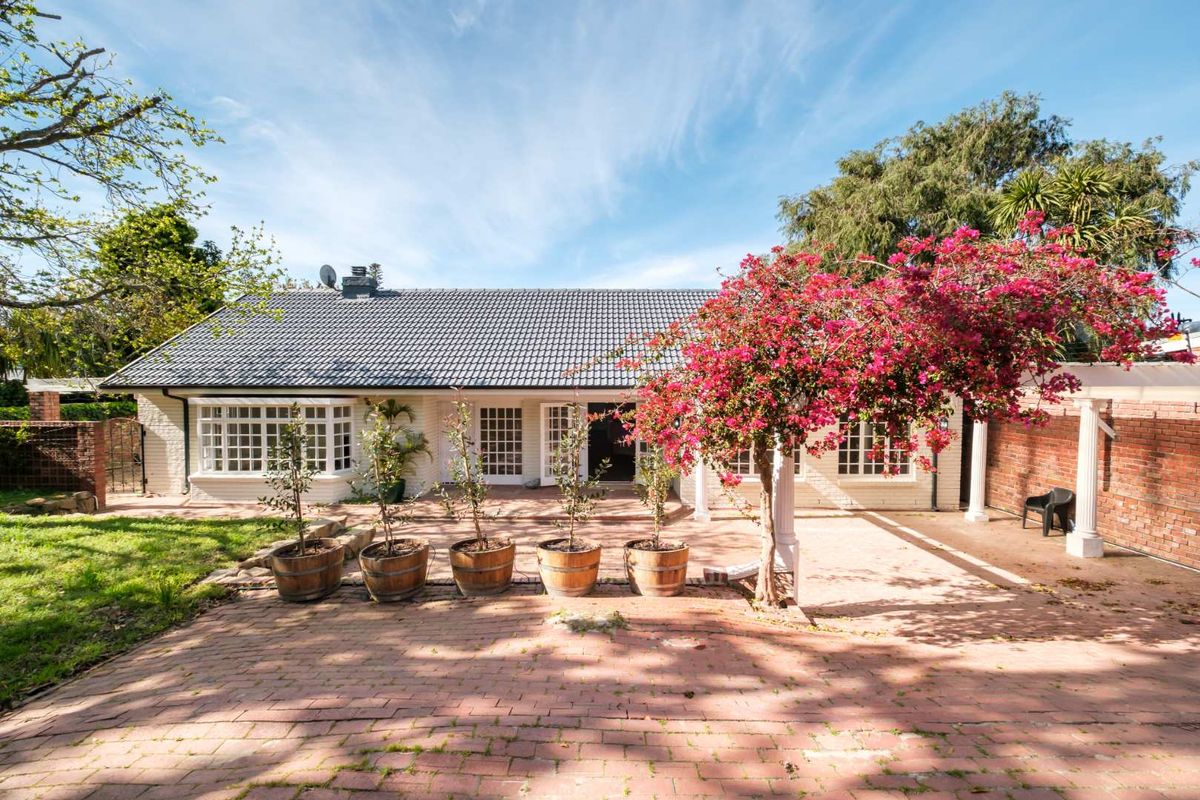 A well-maintained rear exterior view featuring a spacious brick-paved patio, a pergola, and classic french doors leading into the home.