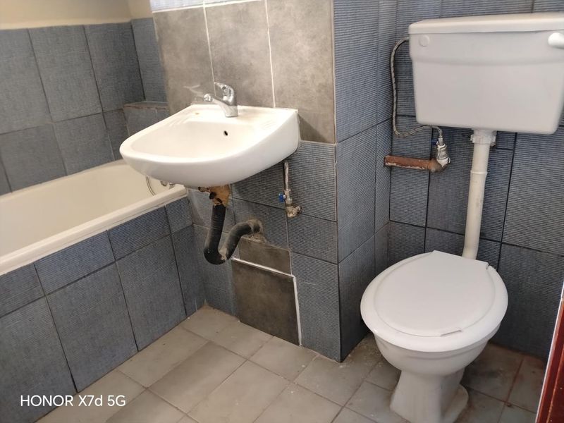 A dated bathroom featuring a wall-mounted basin, bathtub, and toilet with exposed plumbing and tile damage requiring maintenance or renovation.