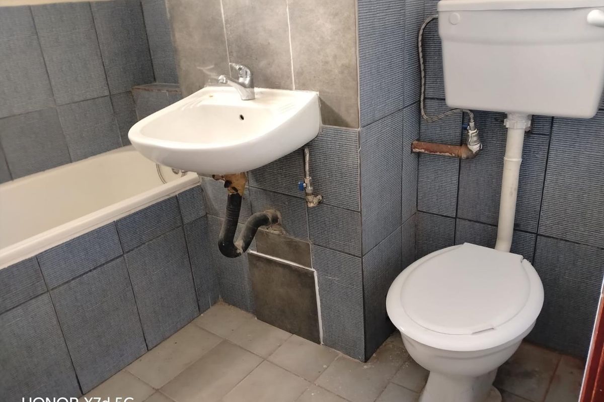 A dated bathroom featuring a wall-mounted basin, bathtub, and toilet with exposed plumbing and tile damage requiring maintenance or renovation.
