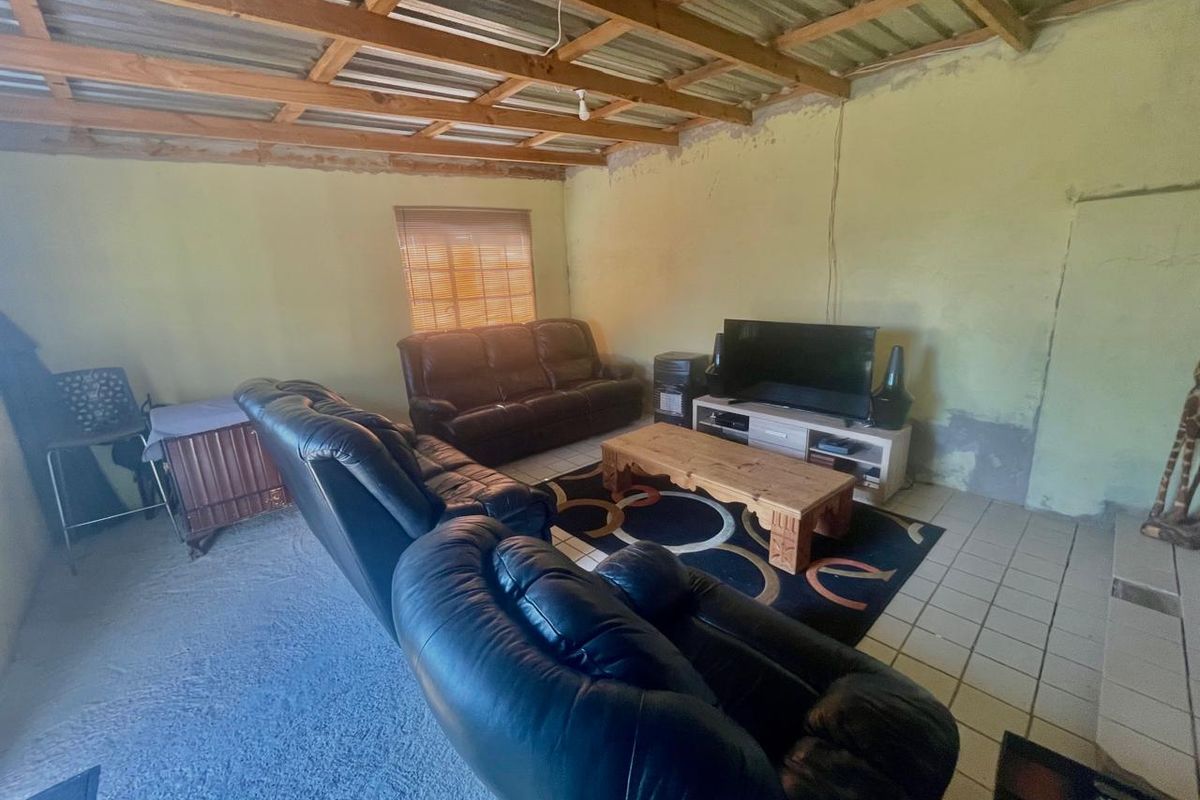 A living room featuring exposed timber roof trusses, corrugated metal ceiling, and tiled flooring, currently requiring wall finishing and maintenance.