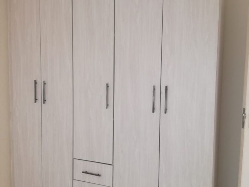 A bedroom featuring light wood-grain built-in wardrobes with integrated drawers and neutral tiled flooring.
