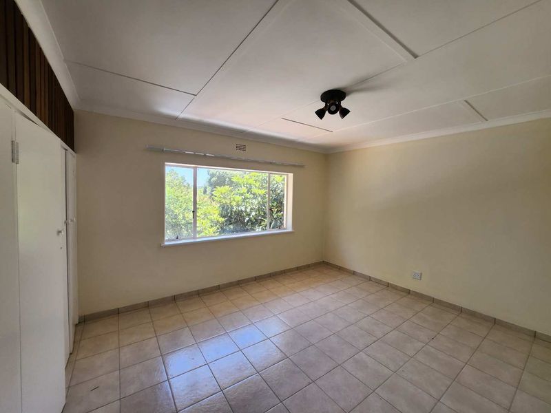 A vacant bedroom featuring tiled flooring, built-in cupboards, and a ceiling fan, offering a blank canvas for potential updates and personalization.