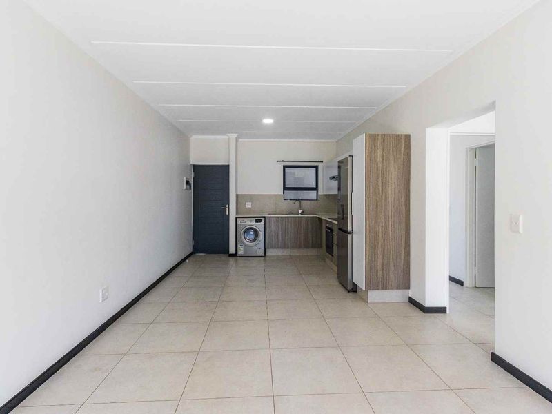 An open-plan kitchen and living area featuring tiled flooring, modern built-in cabinetry, and integrated laundry plumbing in a clean, neutral space.