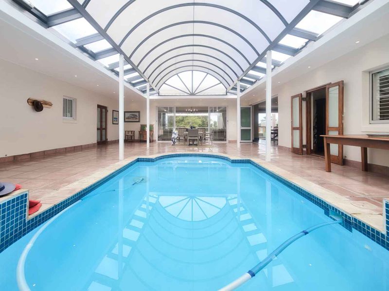 Spacious indoor swimming pool area featuring a striking arched glass roof, tiled flooring, and seamless access to adjacent living spaces.