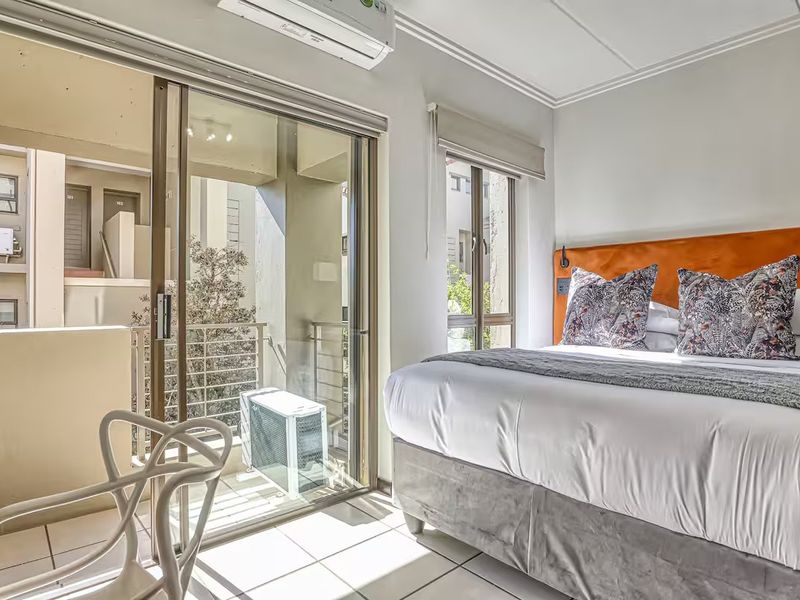A bright bedroom featuring tiled floors, a built-in headboard, and a sliding glass door providing direct access to a private balcony.