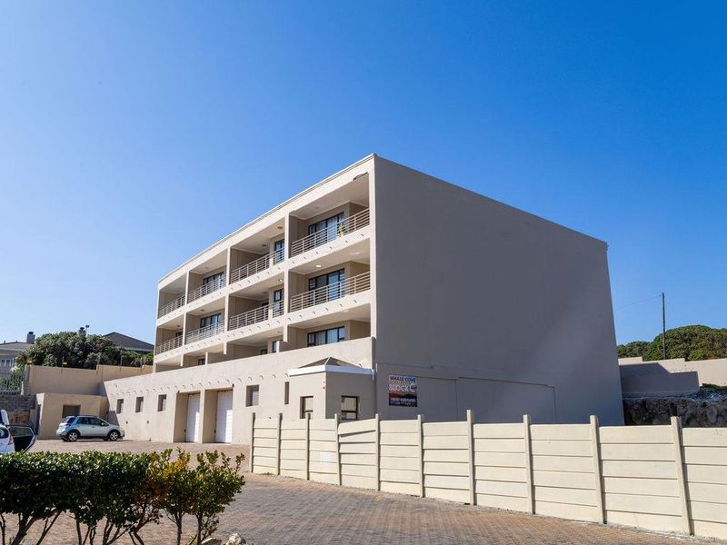 Exterior view of a multi-story apartment building featuring private balconies, sliding doors, and a paved driveway with garage access.